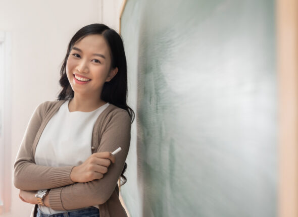Asian Young teacher standing near chalkboard.